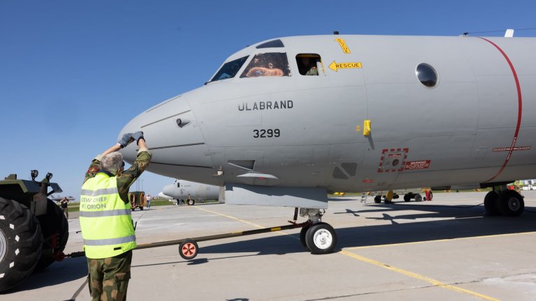 Bakkemannskap i gul vest står og guider et grått fly merket Ulabrand på rullebane