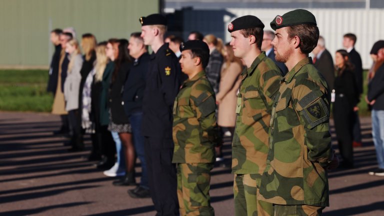 Militære og sivile står oppstilt på en solfylt plass.
