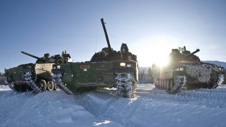 Tre kampvogner står parkert i snødekt landskap med lav vintersol bak