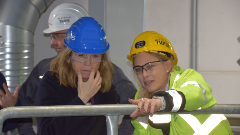 To kvinner med hjelmer fra TKMS ser på noe inne i et teknisk anlegg.