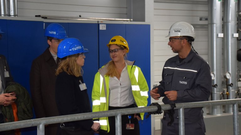 Fire personer med hjelm i samtale inne i et teknisk anlegg.