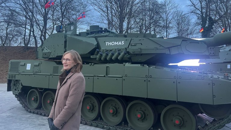 Smilende kvinne står foran stridsvogn