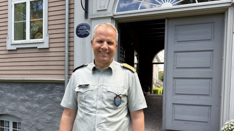 Smilende mann foran trebygning med åpen port
