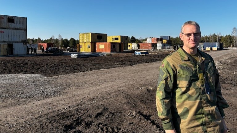 Mann i militær uniform med containere i bakgrunnen.