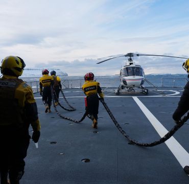 Helikopteret har landet på KV Svalbard for lading av batteri og startstrøm. Isbjørnforskerne har observert flere isbjørn de ønsker å sjekke ut. Flydekkspersonell drar strømkabelen til helikopteret slik at det kan gjøres klart til en tur til. Foto: Forsvarsmateriell  