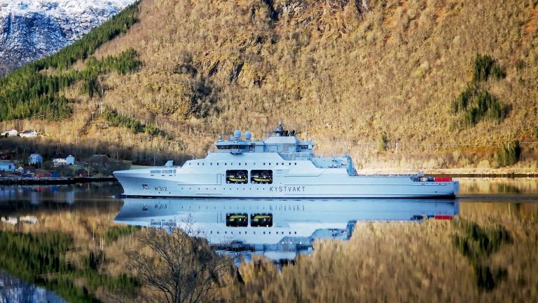 Kystvavktfartøy i stille fjord som speiler seg i vannet